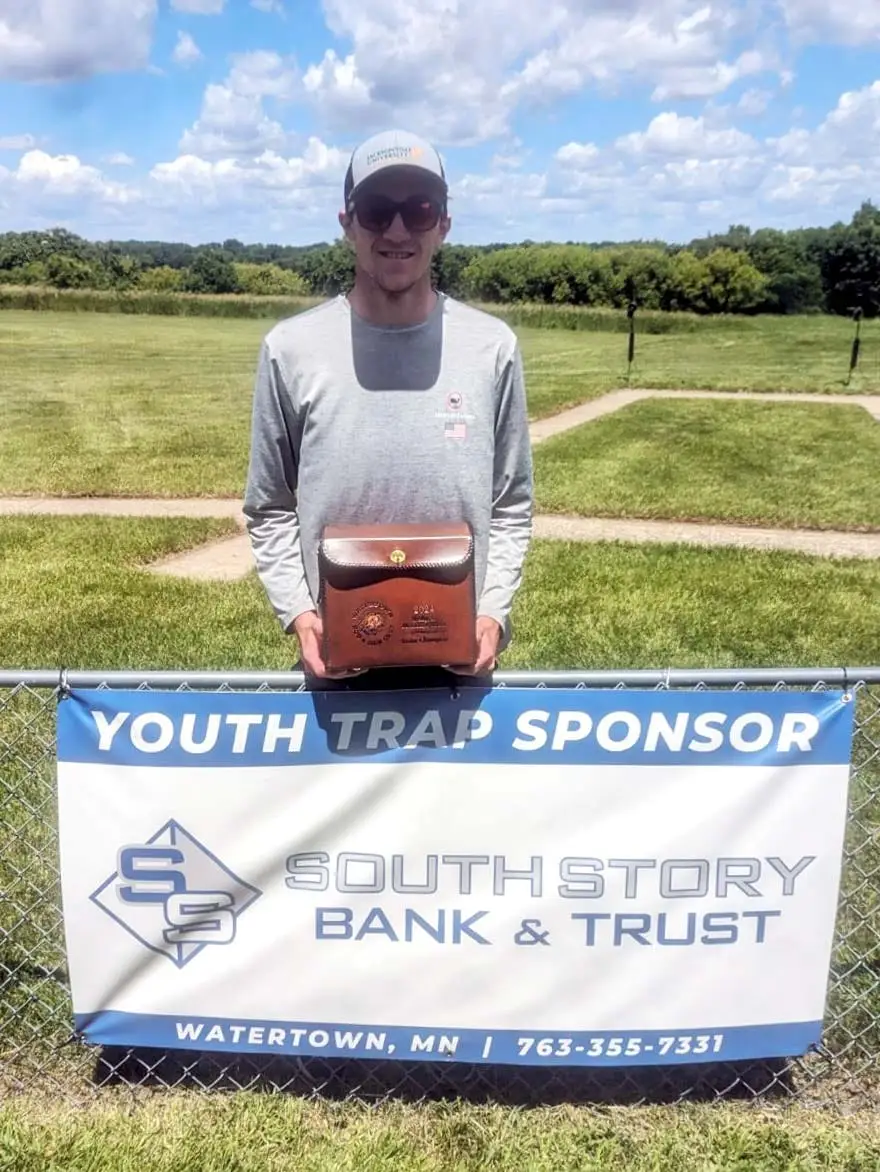 Trap shooting league winner poses in front of South Story Bank and Trust sponsorship banner